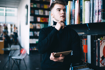 Crop thoughtful man with pen choosing book in library