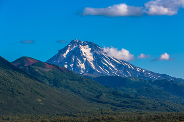 Fototapeta premium View of a mountain valley with a volcano in the background. There is snow on top of the volcano