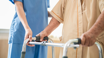 Close up of elderly patient hands using walking frame with nurse assistance. Medical professional...