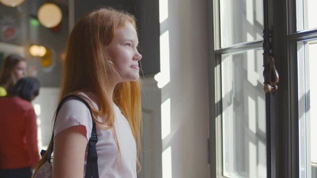 Side view of redhead schoolgirl putting off safety mask during break after classes