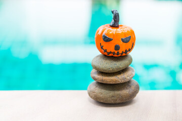 Halloween pumpkin with funny face on stack of stone over blurred blue water background, outdoor day light, happy halloween concept