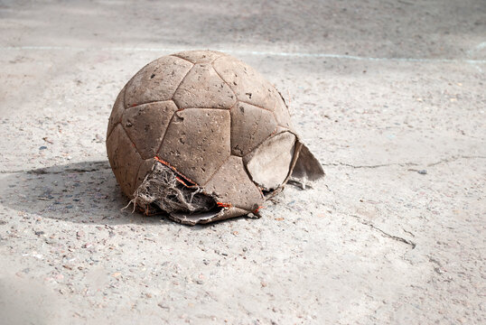 An old, deflated, battered soccer ball with a big hole. On the pavement, place for text