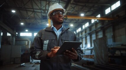 Professional Heavy Industry Engineer/Worker Wearing Safety Uniform and Hard Hat Uses Tablet Computer. Smiling African American Industrial Specialist Walking in a Metal Construction Manufacture. - Powered by Adobe