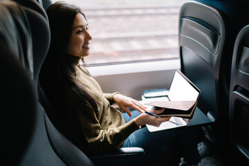Smiling creative female writer enjoying work on journey traveling by train with technology and...