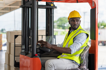 Male worker in safety vest and yellow helmet driving a forklift at warehouse factory