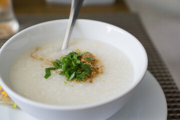 Boiled rice in a white bowl with vegetables sprinkled on top with a spoon, placed on a gray background.