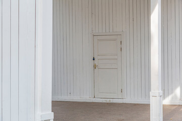 Part of the wall of a white board building with a closed door