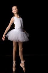 Naklejka premium Cute little girl in a tutu and pointe shoes is dancing in the studio on a black background.