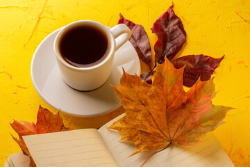 Autumn concept. A cup of espresso, a blank notepad and fall foliage on a yellow concrete table. Close-up. High quality photo