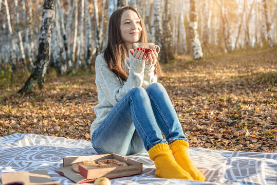 Pretty woman is eating pizza and drinking hot tea in an autumn Park at sunset. Cozy lifestyle in the autumn cold season