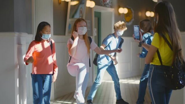 Multiracial schoolchildren wearing facial mask relaxing in school corridor during break