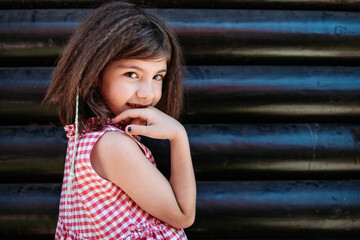 Portrait of a little brunette girl in checkered red dress looking shy