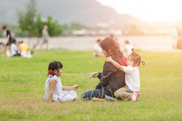 Family at park concept. Mother and her daughter sitting together and play hand at park. Happy family sitting  smiling and relax at park in the evening