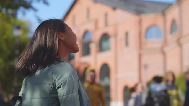 Back view of happy asian schoolgirl standing near building happy to come back after summer holidays