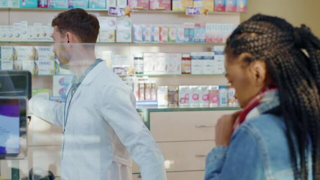 Bearded caucasian pharmacist serving sick female customer in drugstore. Afro-american unhealthy woman listening doctor's advice buying pack of pills. Medication. Health care.