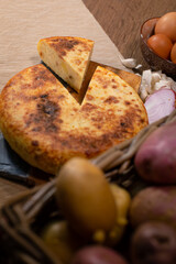 Typical Spanish potato omelette, served at the table with the necessary ingredients for the recipe, potatoes, eggs, onion and garlic