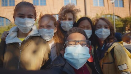 Multiethnic school children wearing protective face masks taking selfie outdoors