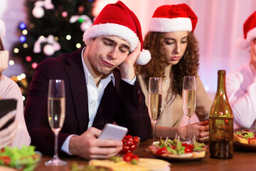 Bored Guy Using Smartphone During Christmas Party With Friends Indoor