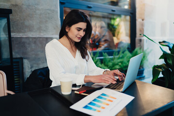 Cheerful woman typing on keyboard of laptop in cafe