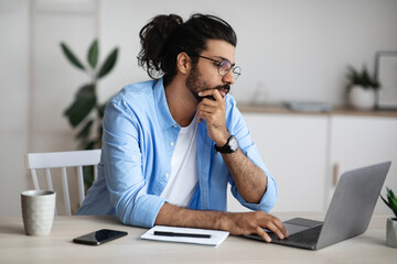 Thoughtful Indian Freelancer Working With Laptop At Home Office, Looking At Screen