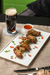 Chicken wings with sesame seeds and glass of dark beer on the table at restaurant