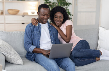 Cheerful black couple using laptop together at home