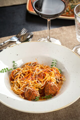 spaghetti with meatballs and tomato sauce and glass of red wine on the table at restaurant