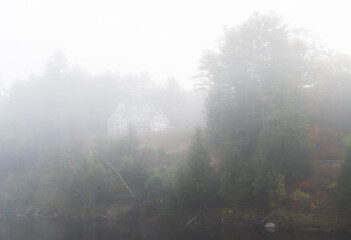 Fototapeta na wymiar Moody and spooky house on the hill covered and hidden in fog and mist, above the Pemi River in New Hampshire.