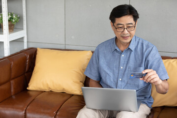 senior asian man using laptop computer for shopping online and paying with credit card