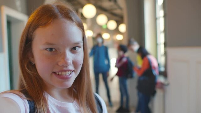 Redhead teenage student girl taking selfie or talking on video call in corridor