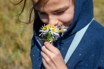 The girl smiles and sniffs the chamomile flowers in her hands