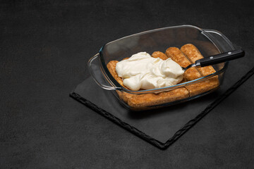 tiramisu dessert cooking - Traditional Italian Savoiardi ladyfingers Biscuits and cream in glass baking dish on dark concrete background