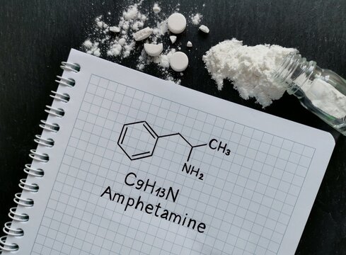 Structural chemical formula of amphetamine molecule with white tablets and pile of white powder in form of amphetamine drugs. Amphetamine (speed) molecule is a central nervous system stimulant.