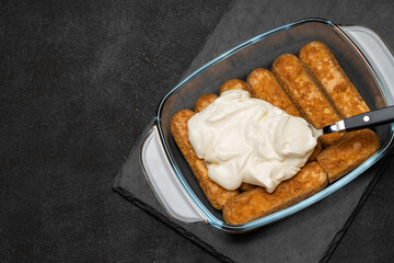 tiramisu dessert cooking - Traditional Italian Savoiardi ladyfingers Biscuits and cream in glass baking dish on dark concrete background