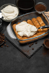 tiramisu dessert cooking - Traditional Italian Savoiardi ladyfingers Biscuits and cream in glass baking dish, coffe maker on dark concrete background
