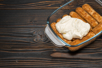 tiramisu dessert cooking - Traditional Italian Savoiardi ladyfingers Biscuits and cream in glass baking dish on wooden background