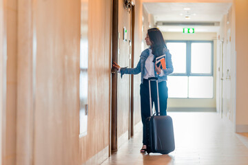 Asian Businesswoman walking with luggage in a hotel corridor and opening hotel room.