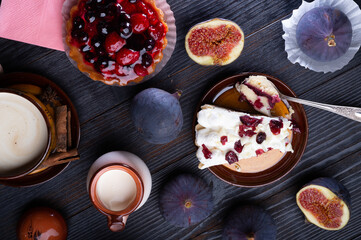 Obraz na płótnie Canvas natural cream, cakes with berries and tasty ripe purple fig on black wooden table. flat lay. life style concept