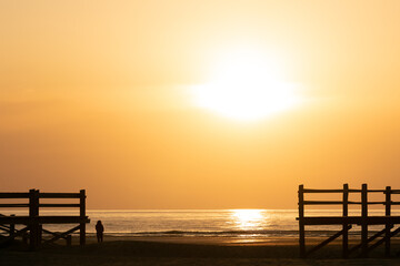 Fototapeta na wymiar Frau steht am Nordsee Strand bei Sonnenuntergang