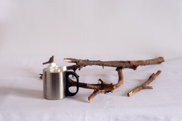 A cup of hot chocolate with marshmallows. On a light background with branches