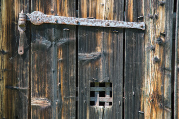 Altes Handwerk: Verwittertes Holztor mit eisernem und rostigem Türbeschlag und Gitterfenster sowie...