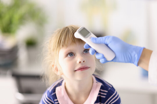 Pediatrician Doctor In Rubber Glove Measures Temperature Of Child With Infrared Thermometer Portrait. Diagnosis And Treatment Of Covid19 In Children Concept.