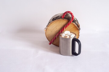 A cup of hot chocolate with marshmallows and Christmas lollipops on a hemp. On a light background