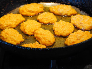 Diet pancakes made from natural pumpkin and millet are fried in a black pan. Home cooking, rustic style