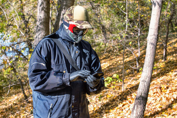 A man wearing a respirator mask and protective glasses using a smartphone walking in the forest at COVID-19 period.