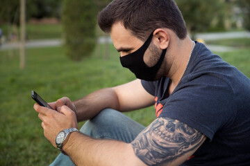 guy with a tattoo typing on the phone, wearing a medical mask