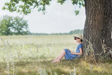 Foto op Plexiglas Leuk meisje geniet van het lezen van een boek onder de boom. Klein meisje voelt zich ontspannen op een mooie zomerdag. © Albert Ziganshin