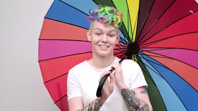 Beautiful young girl with dyed hair and a short haircut. Opens a bright colored umbrella and twists it in front of the camera.