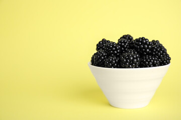 Fresh ripe blackberries in bowl on yellow background. Space for text