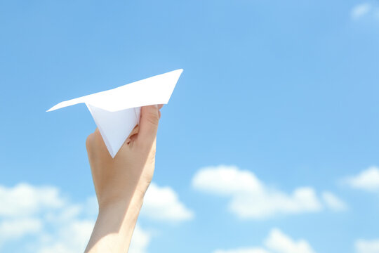 Woman holding paper plane against blue sky, closeup. Space for text